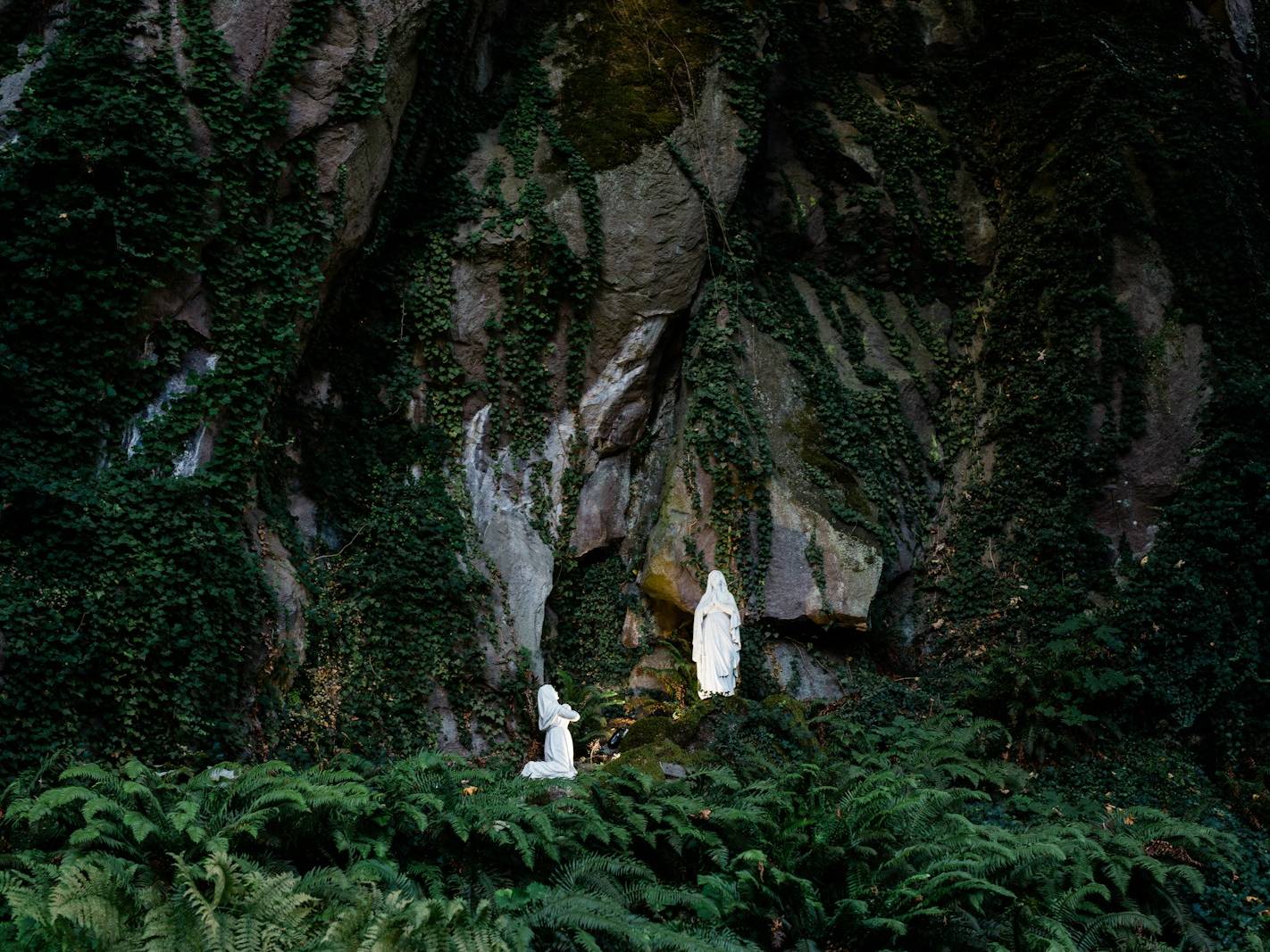person in white shirt standing on green grass near gray rock formation during daytime